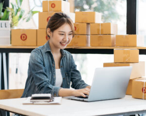 Young business start up online seller owner using computer for checking the customer orders from email or website and preparing packages for product office equipment.
